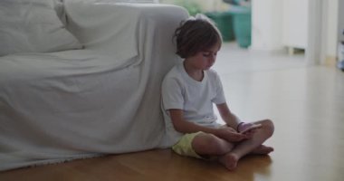 Beyaz bir kanepeye uzanmış bir çocuk, dijital tabletine dalmış, öğle vakti güneşli, modern bir oturma odasında..