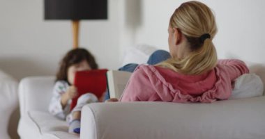 Sarışın bir kadın kitap okurken, küçük bir çocuk da tablet kullanıyor..