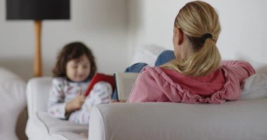 Sarışın bir kadın kitap okurken, küçük bir çocuk da tablet kullanıyor..