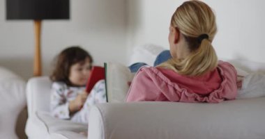 Sarışın bir kadın kitap okurken, küçük bir çocuk da tablet kullanıyor..