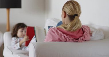 Sarışın bir kadın kitap okurken, küçük bir çocuk da tablet kullanıyor..