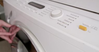 Çamaşır makinesinden bir program seçen bir adam görülüyor. Muhtemelen çamaşır yıkamaya hazırlanıyor..