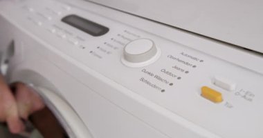 Çamaşır makinesinden bir program seçen bir adam görülüyor. Muhtemelen çamaşır yıkamaya hazırlanıyor..