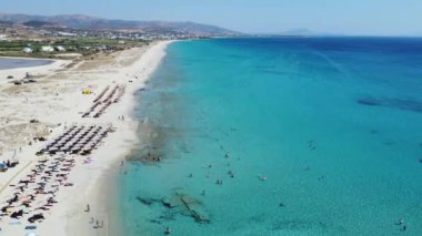 Yunanistan 'ın Naxos kentindeki Agios Prokopios Sahili' nin el değmemiş turkuaz sularını ve kumlu sahillerini, kıyı boyunca dizilmiş şemsiyeler ve güneşliklerle çeken hava görüntüleri.