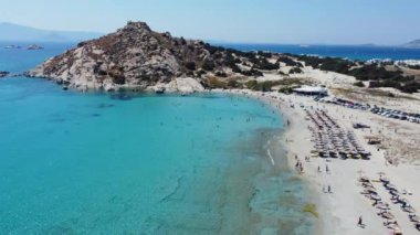 Yunanistan 'ın Naxos kentindeki Agios Prokopios Sahili' nin el değmemiş turkuaz sularını ve kumlu sahillerini, kıyı boyunca dizilmiş şemsiyeler ve güneşliklerle çeken hava görüntüleri.