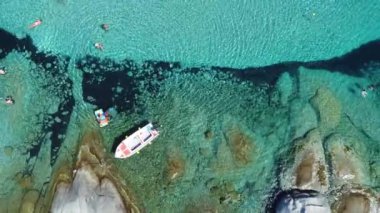 Yunanistan 'ın Naxos Adası' ndaki Plaka Sahili 'nin berrak turkuaz suları ve kayalık kıyı şeridini gösteren bir hava manzarası. Sahne kıyıya yakın bir tekneyi yakalıyor..