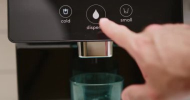 Filtrelenmiş su dağıtım makinesinin soğuk su düğmesine basan bir adamın yakın plan ayrıntıları. Olay yeri muhtemelen kapalı bir yerde gerçekleşiyor ve soğuk, filtrelenmiş suya ulaşmayı içeriyor.