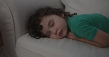 Yeşil tişörtlü kıvırcık saçlı bir çocuk geceleri beyaz bir kanepede mışıl mışıl uyuyor. Huzur ve masumiyet dolu bir an sergiliyor..