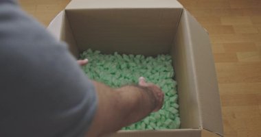 Bir adam yeşil fıstıklarla dolu büyük bir karton kutuyu aramak için iki elini de kullanır..