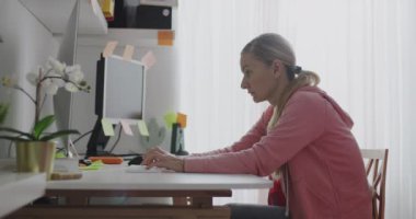 Sarışın kadın ev bilgisayarında çalışıyor, gündüzleri yorgun görünüyor.