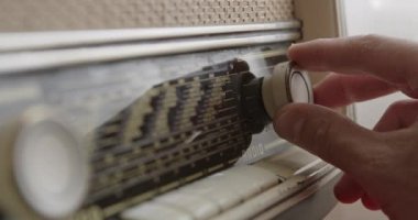 Bir adam eski moda bir radyonun akort kadranını ayarlar ve belirli bir frekans istasyonu bulmaya odaklanır..