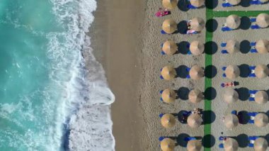 Lefkada, Yunanistan 'da kumlu bir plajda sıralı güneşlik ve şemsiye sergilenen bir hava fotoğrafı. Kristal berraklığında turkuaz sular ve beyaz dalgalar güzel bir kontrast yaratır..