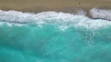 Lefkada, Yunanistan 'da kumlu bir plajda sıralı güneşlik ve şemsiye sergilenen bir hava fotoğrafı. Kristal berraklığında turkuaz sular ve beyaz dalgalar güzel bir kontrast yaratır..