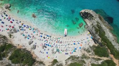Yunanistan 'ın Lefkada kentindeki kalabalık bir plajın yukarıdan aşağı havadan çekilmiş görüntüsü, turkuaz sular ve renkli şemsiyeler sergileniyor.
