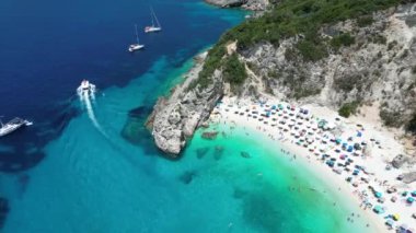 Yunanistan 'ın Lefkada kentindeki kalabalık bir plajın yukarıdan aşağı havadan çekilmiş görüntüsü, turkuaz sular ve renkli şemsiyeler sergileniyor.