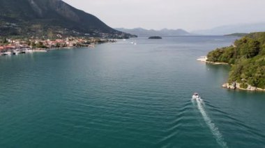 Kıyı koyunda turkuaz sularla yol alan bir teknenin hava görüntüsü. Tekne berrak sularda hareket ediyor, arkasında iz bırakıyor..