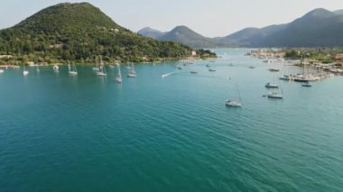 Kıyı koyunda turkuaz sularla yol alan bir teknenin hava görüntüsü. Tekne berrak sularda hareket ediyor, arkasında iz bırakıyor..
