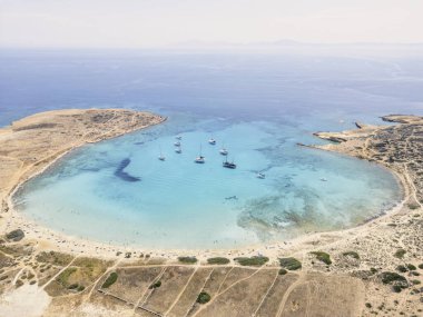 A secluded beach on the island of Koufonisia in the Cyclades, Greece, with crystal clear turquoise waters and a sandy shore. Sailboats are anchored offshore, enjoying the idyllic setting. clipart