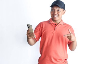 Kırmızı polo tişört giyen mutlu Asyalı adam cep telefonu tutuyor ve beyaz arka planda izole bir şekilde gülümsüyor.