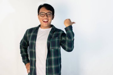 Asyalı gülümseyen genç bir adamın portresi, izole edilmiş beyaz bir arka planda başparmağıyla yan tarafı gösteriyor. Reklamlar, promosyonlar ve sunum modelleri için mükemmel..