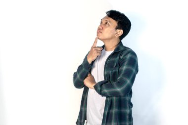 Asyalı bir adam tecrit edilmiş arka planda duruyor, parmak çenesinde şüpheyi düşünüp kafasını kaldırıyor.