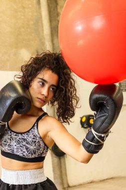 Genç ve güzel bayan boksör kırmızı kum torbasına siyah boks eldivenleriyle vuruyor.