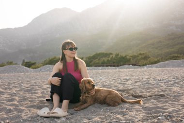 Güzel genç bir kız ve onun cocker spaniel köpeği sıcak bir bahar günü sahilde eğleniyorlar, arka planda dağlar, gün batımı. Yüksek kalite fotoğraf