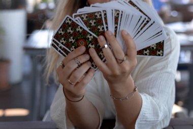 Hafif giysili bir kadın, bir kafedeki masada Tarot kartları okuyor, yakın çekim manzaralı.