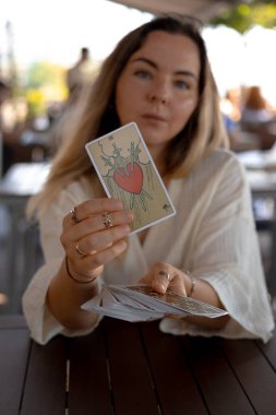 Hafif giysili güzel sarışın kadın kafedeki masada Tarot kartları okuyor.