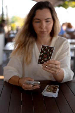 Hafif giysili güzel sarışın kadın kafedeki masada Tarot kartları okuyor.