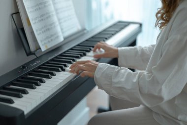 Beyaz elbiseli genç bir kadın oturuyor ve elektronik piyano çalıyor.. 