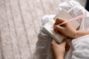 Yakın plan, genç bir kadın evdeki kanepede otururken not defterine not alıyor.