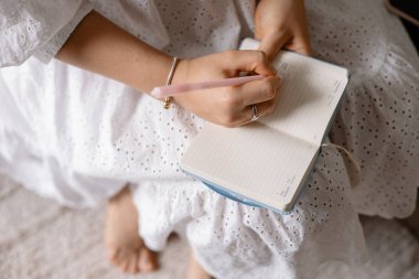 Yakın plan, genç bir kadın evdeki kanepede otururken not defterine not alıyor.