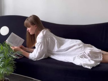 Kadın evde kanepede kitap okuyor, dinleniyor ve rahatlıyor.