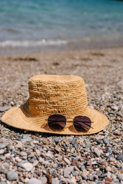 Hasır şapka ve güneş gözlükleri kumsalda, yaz mevsiminde.