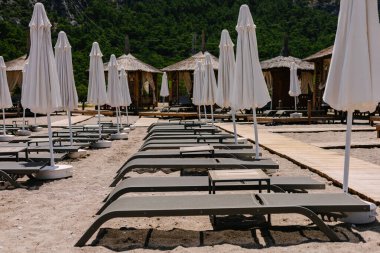 Güneşli şezlongları, masaları ve beyaz şemsiyeleri olan güzel boş kumsal, yaz.