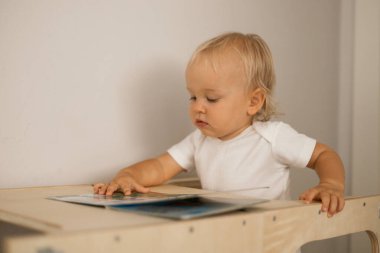 Küçük güzel sarışın kız, evdeki ahşap çocuk masasında oturan kitaba bakıyor.