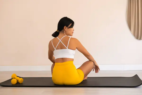 Çekici Asyalı spor eğitmeni spor salonu ve yoga stüdyosunda kamera karşısında oturuyor. Sarı ve beyaz spor giyim. Eğitimden sonra dinleniyorum. Boşluğu kopyala