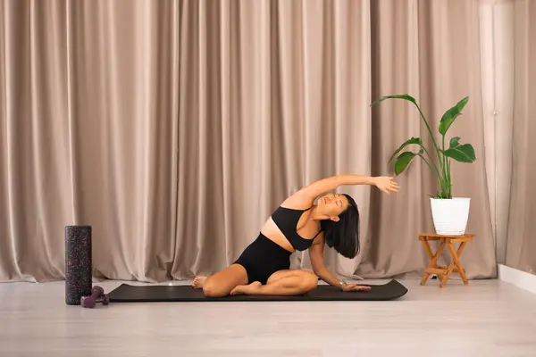 Sportif Asyalı kadın siyah yoga minderi üzerinde soyunma egzersizleri yapıyor ve stüdyoda köpük rulo, fitness, pilates, sağlık ve aktif yaşam.