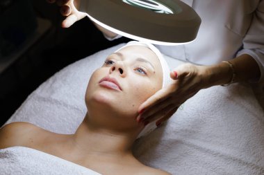 Klinikteki kozmetoloji dolabında güzellik prosedürü. Beyaz üniformalı bir terapist ve arabada yatan bir müşteri. Estetik stüdyosundaki modern ofis.