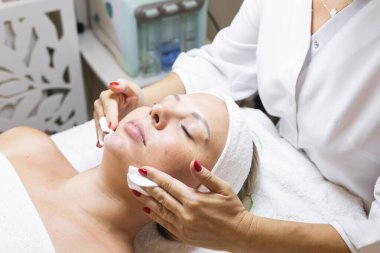 Güzellik stüdyosunda kozmetoloji prosedürü. Eller yakın çekim, modellerin yüzüne temizleyici jel uygulanıyor.