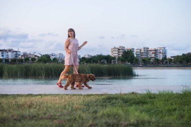 Güzel genç bir kadın Cocker Spaniel köpeğiyle nehir kıyısında yürüyor. Güzel şehir arkaplanı
