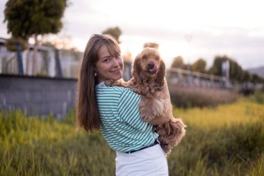 Genç ve güzel bir kadın ve cocker köpeğinin portresi, halk parkında yaz günbatımı.