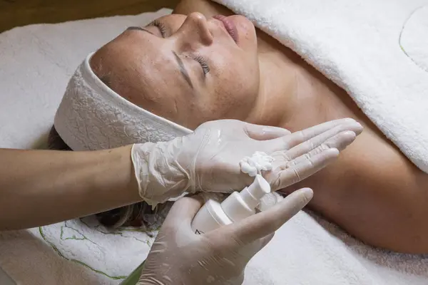Güzellik stüdyosunda kozmetoloji prosedürü. Beyaz eldivenli yakın çekim eller, modellerin yüzüne krem sürüyor. Klinik
