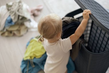 Çamaşır sepeti ve sarışın çocuk, gelişim ve büyüme ile temizlik yapmayı öğrenmelerine yardımcı oluyor. Dairedeki temizlikçilerle yıkamak için kıyafetleri olan çocuk portresi..