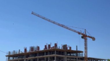 Bir inşaat vinci, çok katlı yeni bir bina veya evin inşaatı sırasında inşaat işi yapıyor. Güneşli yaz günü ve mavi gökyüzü