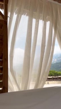 Bir yaz plajı ahşap çardağı veya çadırında şeffaf dalgalı perdeler, aydınlık, dinlenme, rahatlama ve lüks bir atmosfer, güneşli bir gün ve hafif bir rüzgar, Türkiye 'nin Antalya kentinde bir plaj. Dikey video
