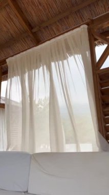 Bir yaz plajı ahşap çardağı veya çadırında şeffaf dalgalı perdeler, aydınlık, dinlenme, rahatlama ve lüks bir atmosfer, güneşli bir gün ve hafif bir rüzgar, Türkiye 'nin Antalya kentinde bir plaj. Dikey video