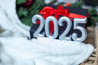 Gri sayılı tatil kartı 2025, Noel ve Yeni Yıl kutlamaları, gümüş figürler, yumuşak beyaz ekose, kırmızı fiyonklu siyah hediye kutusu ve arka planda Noel ağacı, kopyalama alanı