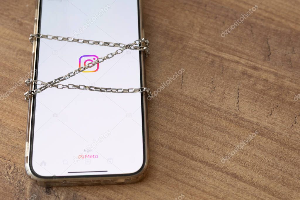 Turkey, Antalya - August,2 2024: A mobile phone screen with social media icon of Instagram on it. Wrap the phone in a chain. The concept of limiting time on social networks, banning in country or